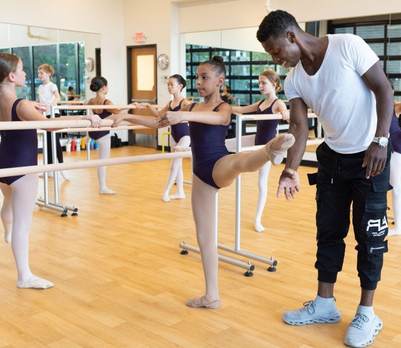 A Dance teacher helps a younger student at the barre